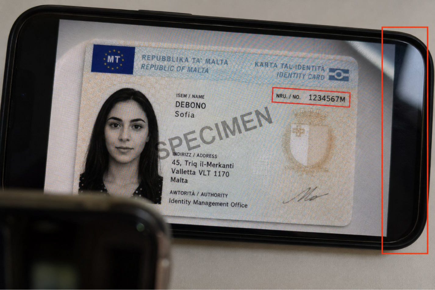 A Maltese identity card photographed off a second phone screen, with screen edges highlighted — not a real document.